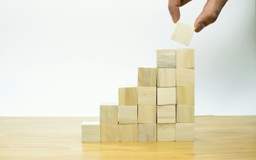 Eine Hand baut eine Pyramide aus Holzwürfeln.